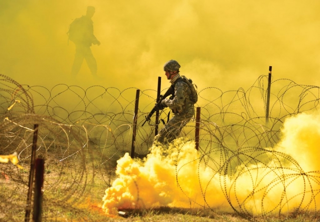 An Oregon Army National Guard Soldier proceeds through a combination of thick smoke, tear gas and razor wire as their unit mentor watches from above, during the 2017 Oregon Best Warrior Competition at Camp Rilea, near Warrenton, Ore. Soldiers compete in a variety of warrior tasks to determine which Soldier and NCO will represent Oregon at the regional-level competition.