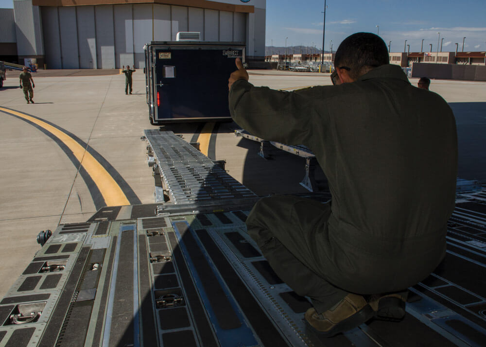 A loadmaster from the 452nd Airlift Wing guides a vehicle and trailer onto a C-17 Globemaster cargo aircraft at Goldwater Air National Guard Base.