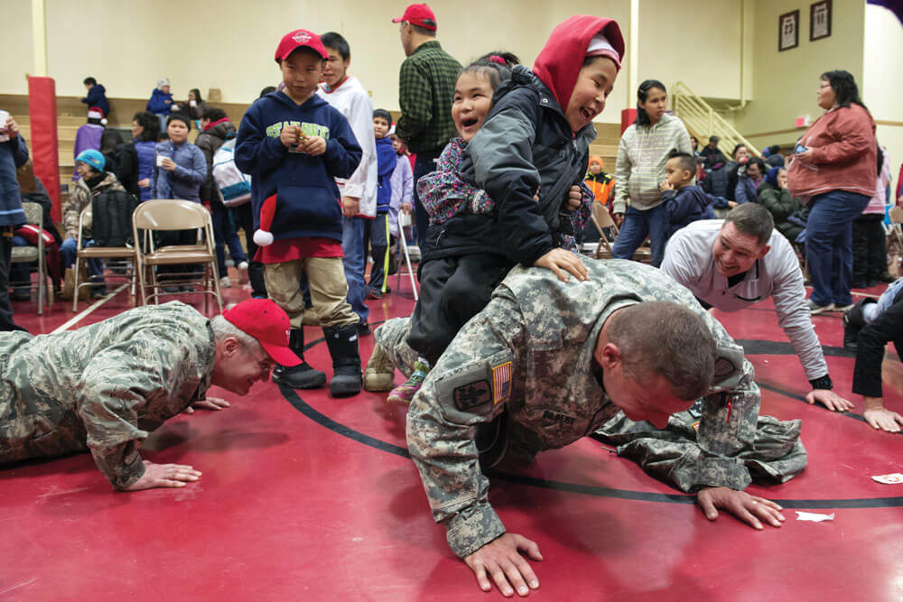 Children from St. Mary’s, Alaska, test Alaska Army National Guard LTC Joel Gilbert’s strength by sitting on his back while he does push-ups during Operation Santa Claus 2015.