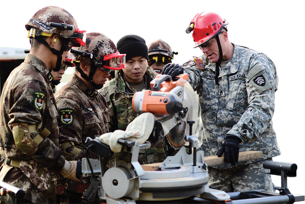 SSG Jason Cushman, 442nd Engineer Utility Detachment, Oregon Army National Guard, assists Joint Logistics Force soldiers from the People’s Liberation Army as he uses a saw to cut wood for shoring structures. Oregon Army National Guard photo by SFC April Davis.