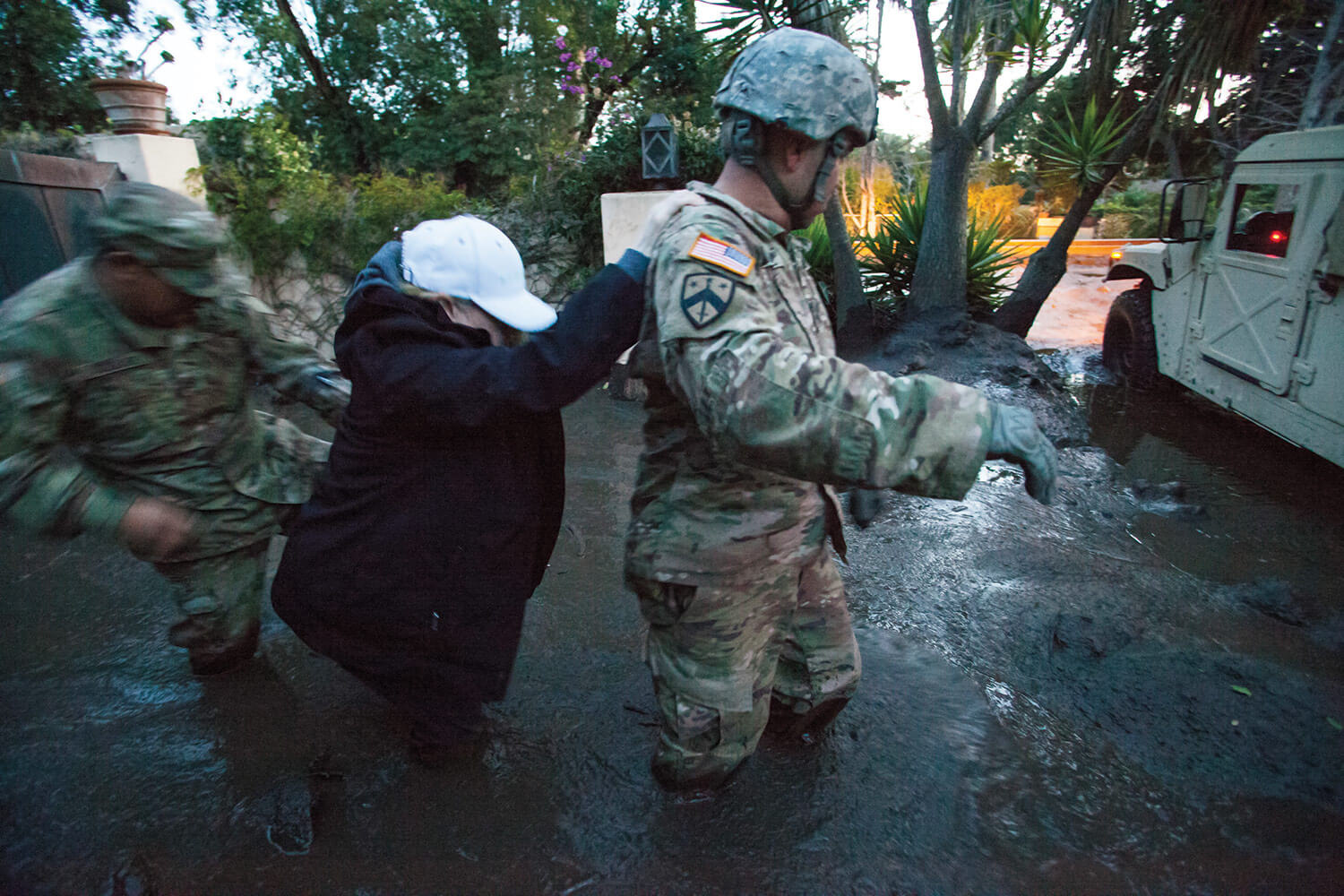 SGT Jose Paiz (right) and SSG Michael Aguilar both of the 1114th Composite Truck Company, California Army National Guard, guide a resident through thick, knee-deep mud from a Montecito, Calif., home to the Soldiers’ HMMWV. The 1114th is credited with rescuing or evacuating more than 1,800 citizens in the Montecito area following the deadly mudslide that struck the city in the predawn hours of Jan. 9, 2018. California National Guard photo by SrA Crystal Housman.