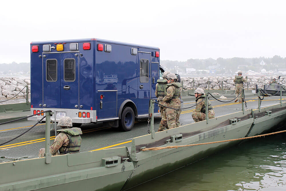 Soldiers from the 1437th Multi-Role Bridge Company guide an ambulance and crew from the 51st Civil Support Team to a designated area before maneuvering the 130-foot ribbon bridge into the waters of the Straits of Mackinac. Michigan National Guard photo by Scott Martzke.