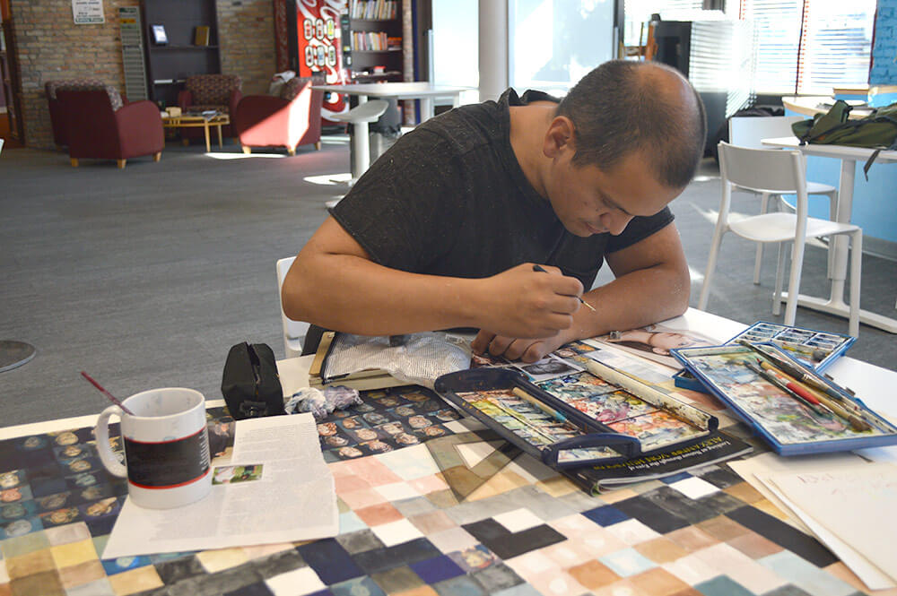 SPC Cole LaRocque at work on a large watercolor featuring over 1,000 faces. Photo courtesy SPC Cole LaRocque