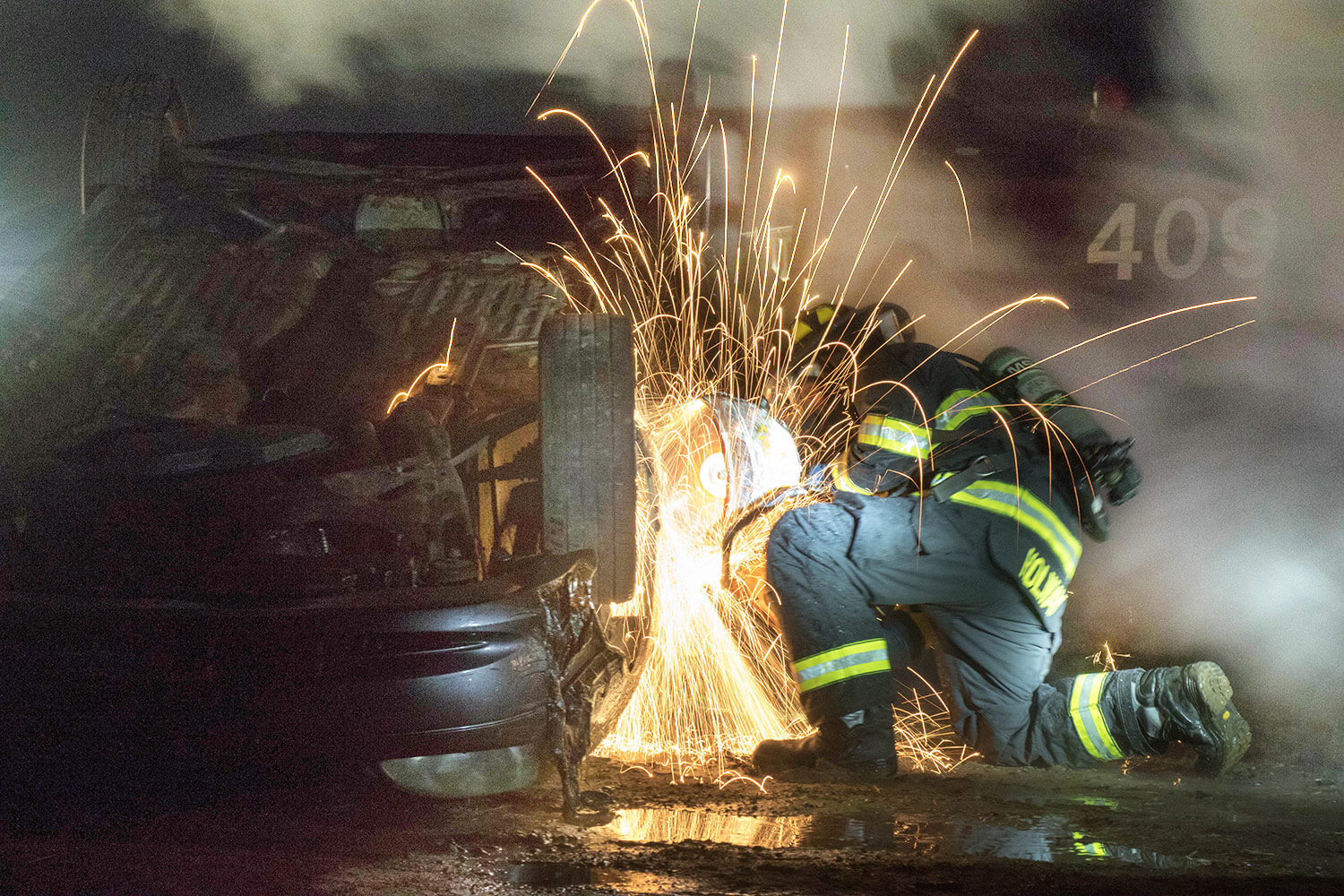 A Soldier with the 79th Engineer Company (Firefighting), Massachusetts Army National Guard, uses a circular saw to cut through a car door during a training exercise at Tactical Training Base Kelley on Joint Base Cape Cod, Mass. The training required Soldiers to ascertain the best method to evacuate dummies from a vehicle that was flipped and burning in the night. Massachusetts Army National Guard photo by PFC Sean Park