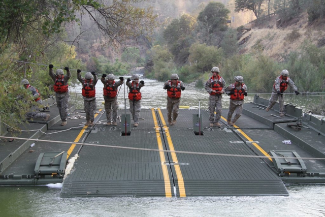 A launch and retrieve team from the 132nd Multirole Bridge Company (MRBC), 579th Engineer Battalion, 49th Military Police Brigade, California Army National Guard, uses a steel guideline to move a ramp-and-bay over Cache Creek River in Cache Creek Regional Park, Yolo County, Calif. The platforms are part of a floating bridge constructed by the MRBC to help California Department of Forestry and Fire Protection vehicles and equipment cross the river to battle wildfires. California Army National Guard photo by SSG Eddie Siguenza