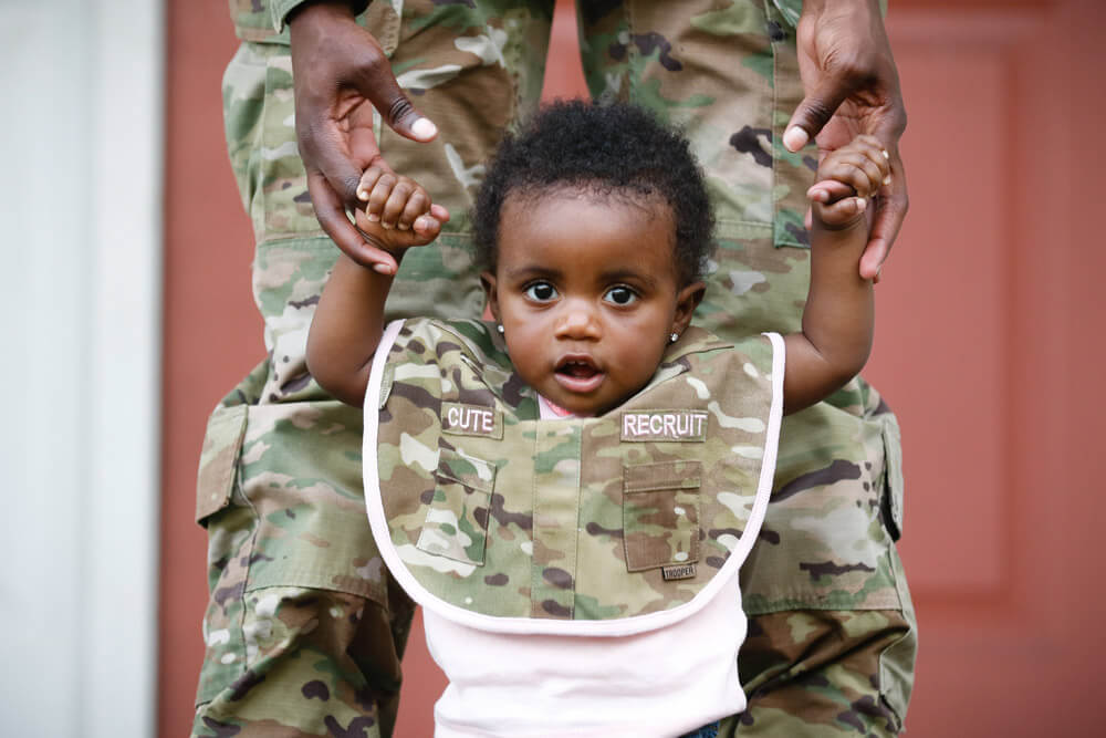 Amore Cox stands with the help of her mother, SPC ShaTyra Reed, a public affairs mass communications specialist with the 22nd Mobile Public Affairs Detachment, XVIII Airborne Corps Headquarters and Headquarters Battalion, in Fayetteville, N.C. U.S. Army photo by PFC Hubert D. Delany III