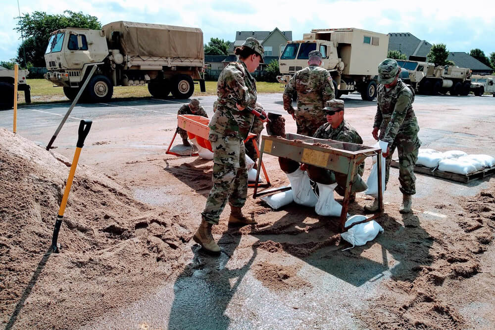SPC Jessica Post (left), a member of the 120th Medical Company, Oklahoma Army National Guard, shovels sand into a manual sandbag filler with the aid of fellow Soldiers in Bixby, Okla., during flood relief efforts, May 2019. Oklahoma Army National Guard photo by SPC Jessica Todd